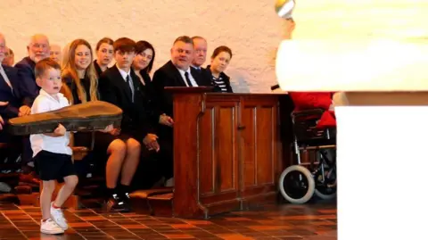 Gleeson Family  A young boy carrying a fiddle up a tiled floor at a funeral