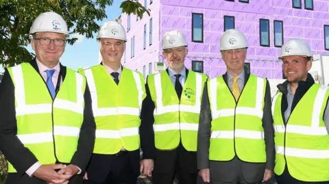 East Suffolk and North Essex NHS Foundation Trust Men in high-visibility suits and white hard hats standing in front of a building
