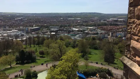 A picture of Brandon Hill from above with trees and grass paved with a brown path. The skyline shows Bristol city.