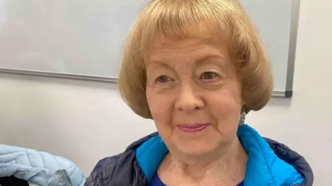 A woman with her hair cut in a bob wears a bright blue and dark blue anorak.