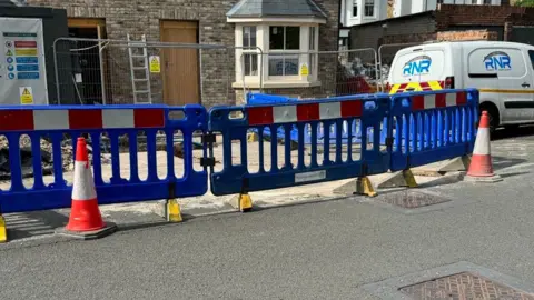 Roadworks in Guildford. Blue plastic fencing around where works are happening with red traffic cones. A white van can be seen in the background