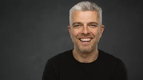 Evangelical Alliance Peter has a full head of short grey hair, lifted at the front. He is wearing a black t-shirt and smiling. 