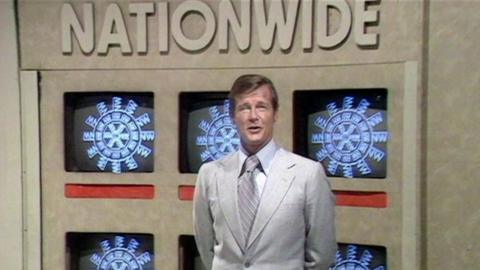Roger Moore stands against a background of televisions, that say Nationwide