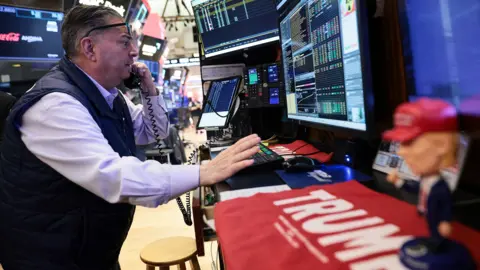 Michael M. Santiago / Getty Images A trader at the New York Stock Exchange talks on the phone while gesturing in front of screens with stock market numbers on, and a toy doll of Donald Trump on the desk in front of him, in New York on Wednesday.