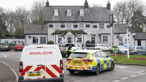 PA Media Two police vehicles are parked outside a white pub. 