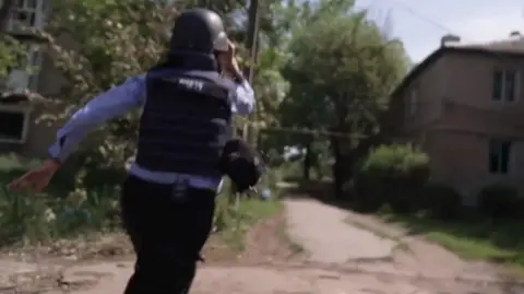 Yogita Limaye running from a drone attack. She is wearing a helmet and press vest.