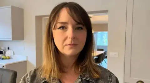 A woman with long blonde hair and a denim jacket in a room with white walls
