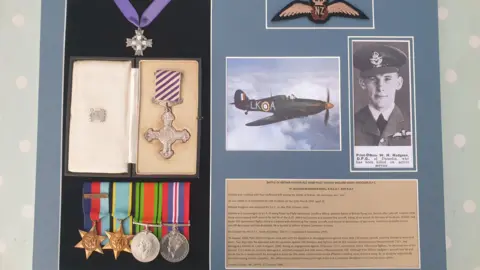 Kent Battle of Britain Museum A Battle of Britain medal set on display. There is a black and white photograph of a New Zealander pilot.