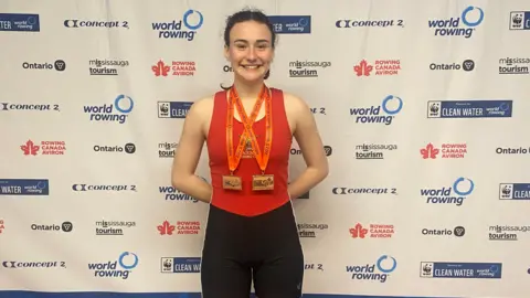 Supplied A woman wearing red vest and medals in front of a world rowing championships backdrop