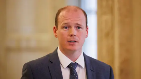 PA Media Gordon Lyons. He is balding, wearing a dark blue blazer, white shirt and dark blue polka tie.
