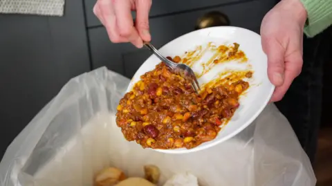 Getty Images Woman scraping leftover curry off a plate into a bin