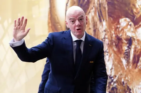 Gianni Infantini, wearing a suit, holds up his hand