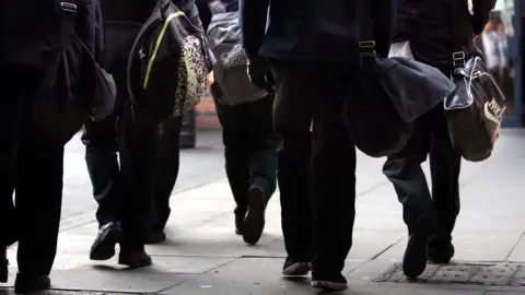 Behind a group of young people walking with school bags. 