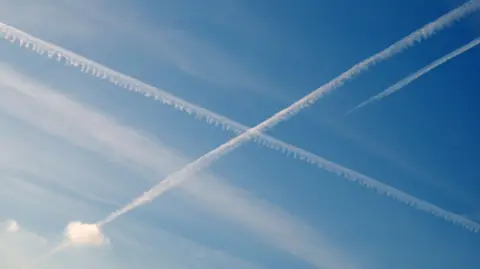 Two contrails, white plumes of cloud caused by aircraft, crossing in mid-air against a blue sky