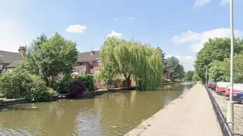 Canal towpath running past trees in a built up area