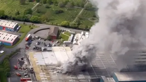 Image taken from a helicopter shows smoke rising from the Warburtons factory in Burnley. A large column on grey smoke rises from the roof the building. 