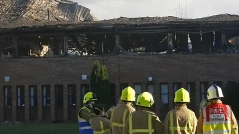 Reuters Firefighters look on at the destroyed SODC building, which is clearly burned on its top floor and it appears its roof has caved in.