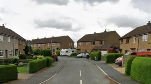 Google Semi-detached houses run along either side of the street, with hedges to the left and right.