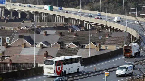 Getty Images Cars, a bus, a dustbin lorry and vans on the M4 motorway flyover at Port Talbot as it passes by terraced houses
