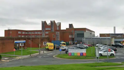 The exterior of Furness General Hospital. It is a red-brick building with cars parked at the front.