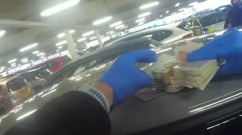 Police body cam footage showing a police officer wearing blue plastic gloves holding wads of cash