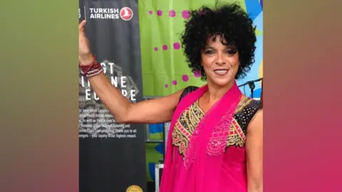 Carolyn Stewart A woman, Carolyn Stewart at Belfast Mela. She has dark curly hair and is wearing a hot pink dress.
