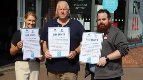 Rushcliffe Borough Council Three people holding up signs for safe spaces in the Nottinghamshire borough of Rushcliffe.