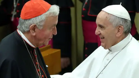 EPA Cardinal Vincent Nichols, wearing a red cap and black cassock, smiles at Pope Francis, wearing a white hat and white cassock