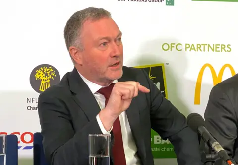 PA Media Steve Reed at a press conference, speaking against a backdrop with the NFU logo behind him