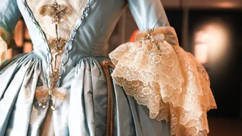 Closeup of one of the gowns in the exhibition. It is a blue and gold eighteenth-century-style ballgown.