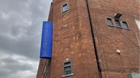 Image shows the blue Odeon sign at the closed cinema on George Street, in Oxford. The lettering has been removed. In the background is a stormy sky.