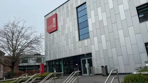 A large grey building with a red sign in the corner that says Staffordshire University.