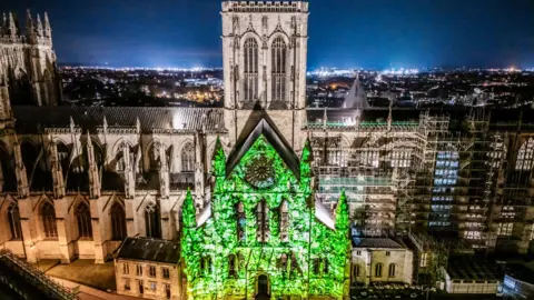 PA Media A wide image of York Minster at night, with a large projection of green light on one side of the building.
