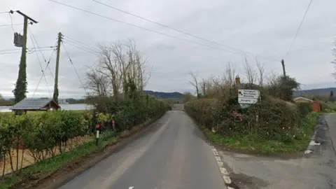 Google A Googlemap snip of a road junction in a rural area. A roadsign can be seen pointing to the villages of Burghill. Hedges line the roads and properties can just be seen over the tops of hedges. The picture is taken on a grey day.