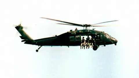 AFP A Black Hawk helicopter flies in the sky. Four soldiers can be seen sitting at the door of the vehicle.