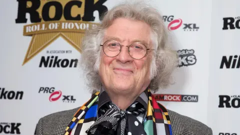 A man with grey hair and glasses is smiling at the camera. 