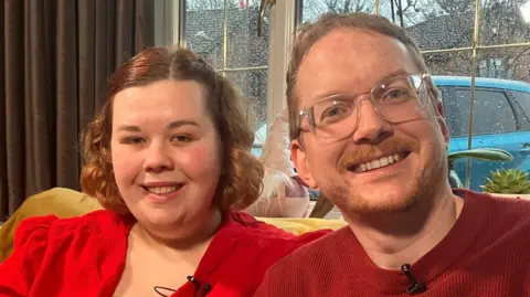 Emma and Mike Stock next to each other and smiling. They are both wearing red.
