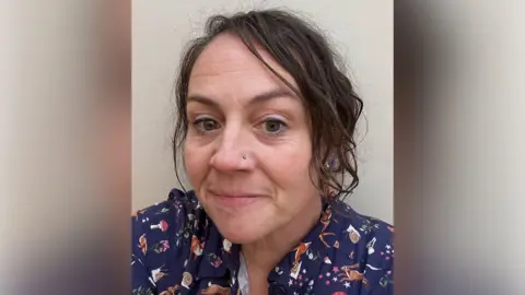 Kettering General Hospital Dr Herbert with medium-length dark hair and a nose stud looking at the camera. She has a blue shirt with animal-related designs on it.