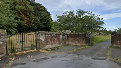 Google A sandstone wall entrance to Grange Cemetery with two black metal gates