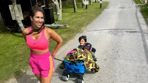 Raina Heverin A woman in activewear pulling her children in a small trolley behind her. 