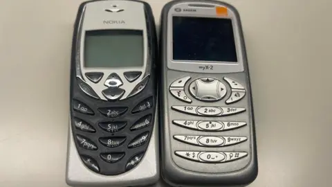 Two brick phones sit next to each other, one a black and silver Nokia and the other a gray-silver Sagem myX-2.