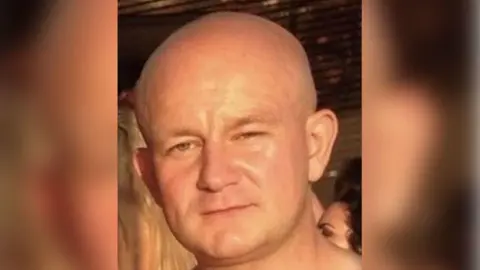 Merseyside Police Dylan Bacon, who has a bald head, looks directly into the camera