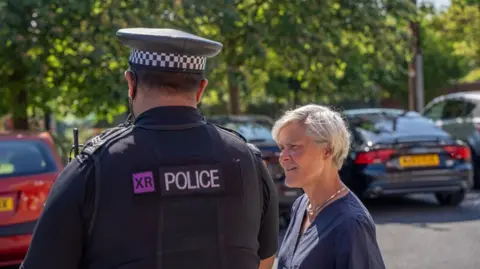 Greater Manchester Combined Authority A woman with short blonde hair appears to be in conversation with a police officer in a car park 