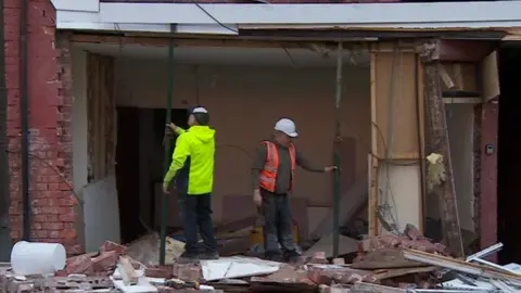 Two men in protective gear putting in poles to shore up the second storey of a building following an explosion