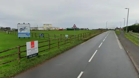 Dunkeswell Aerodrome. A wooden fence is around the perimeter. A sign for the aerodrome is in the field.
