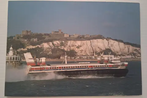 English Heritage A postcard showing a large hovercraft on the sea with the white cliffs of Dover and Dover Castle visible behind it.