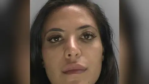 A custody mugshot of Anita Mirmohammadi. She has dark hair and a blank expression on her face.