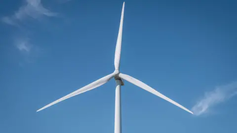 A single white wind turbine against an almost cloudless blue sky