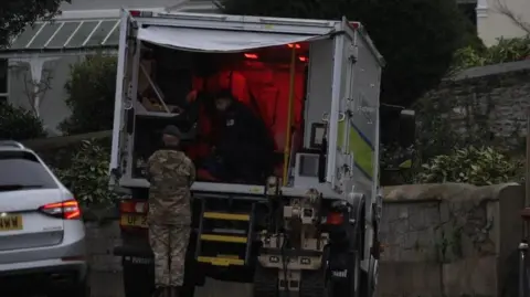 A Royal Navy officer in camouflage standing outside a van with another officer inside