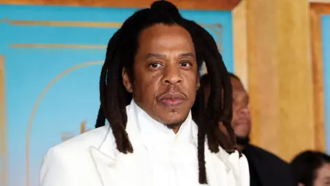 Jay-Z is photographed at a movie premier wearing a white suit 